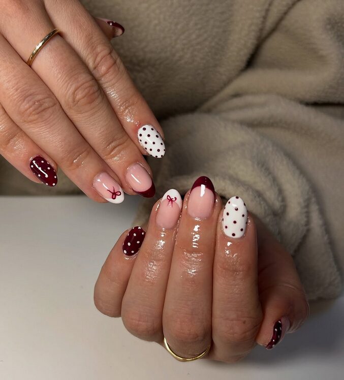 Deep burgundy nails with crisp white and gold polka dots and tiny bow accent