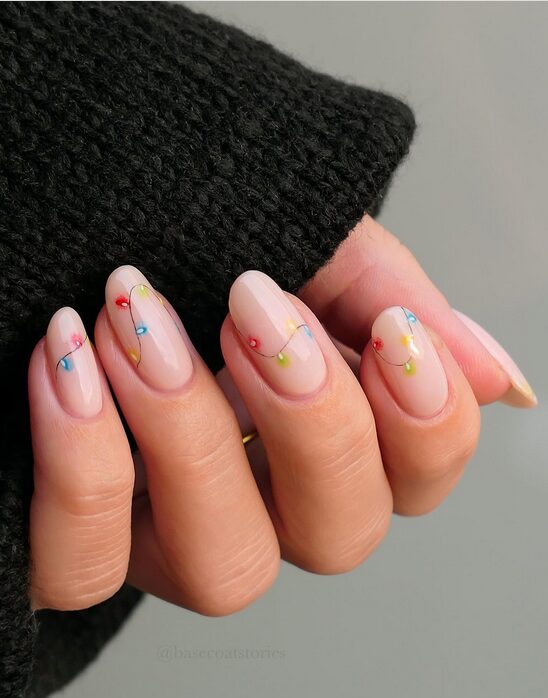 Clear hard-gel nails with tiny glowing holiday light-string effect in red, green, and gold wrapped around each nail