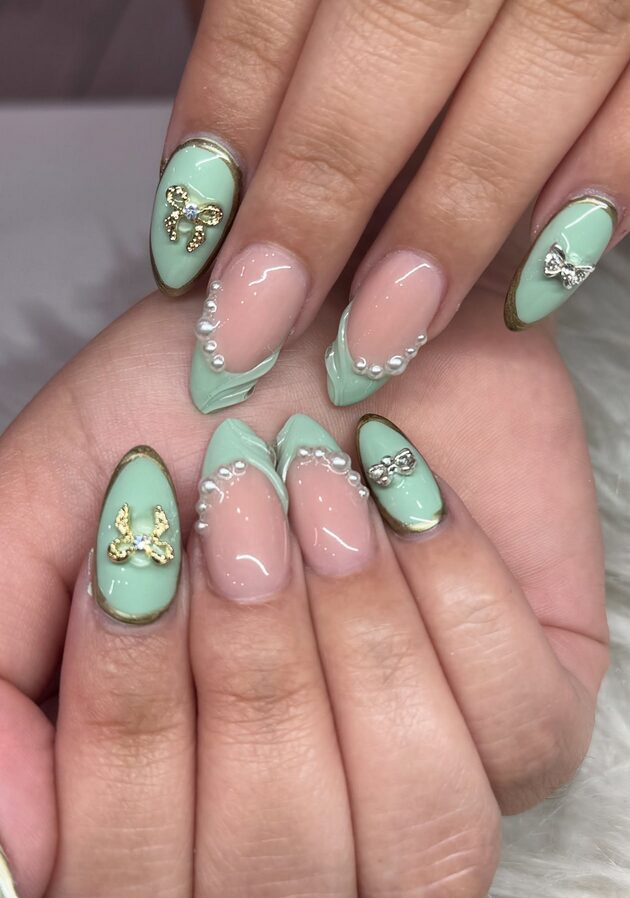 Pastel green almond nails with small pearl accents near cuticle