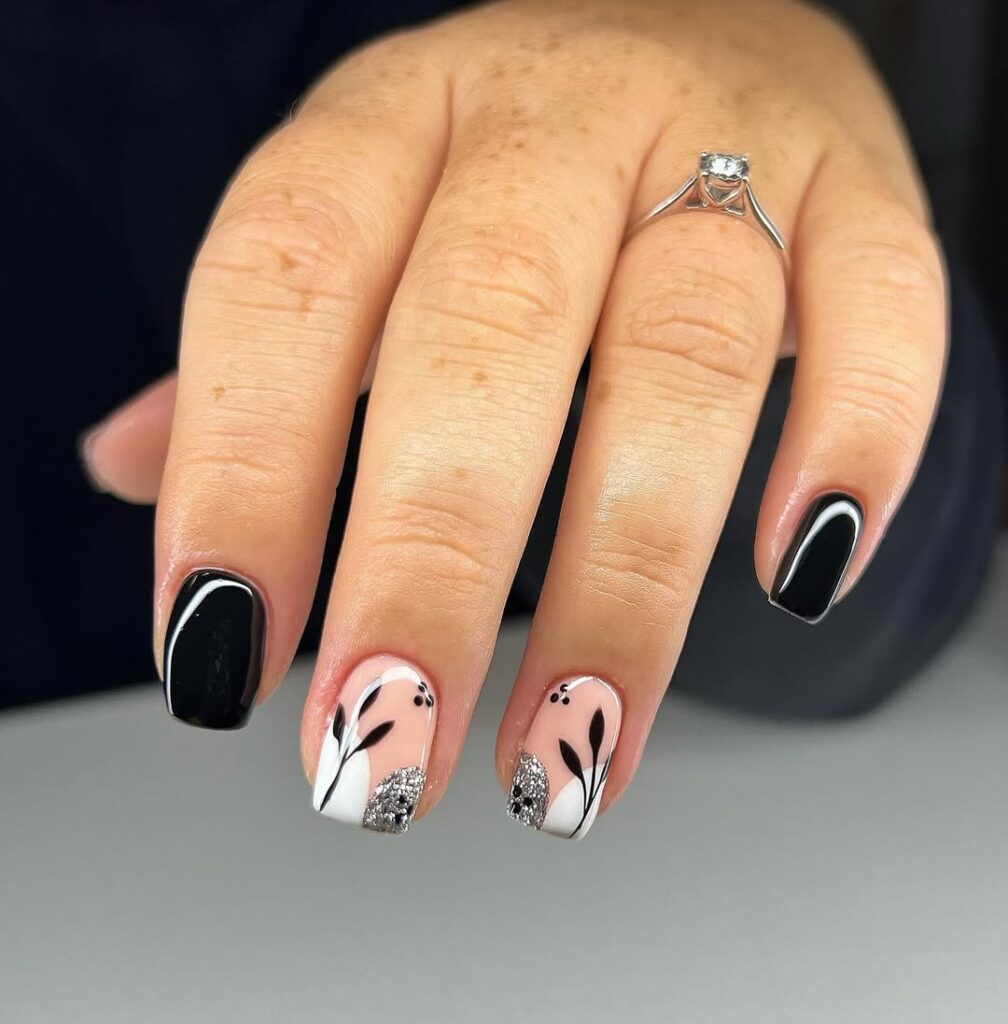 Black nails with white floral accents and silver glitter