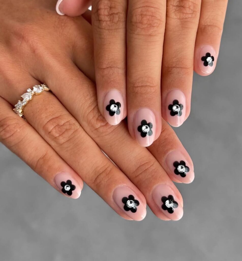 Sheer nude nails with black daisy flowers and crystal rhinestone centers