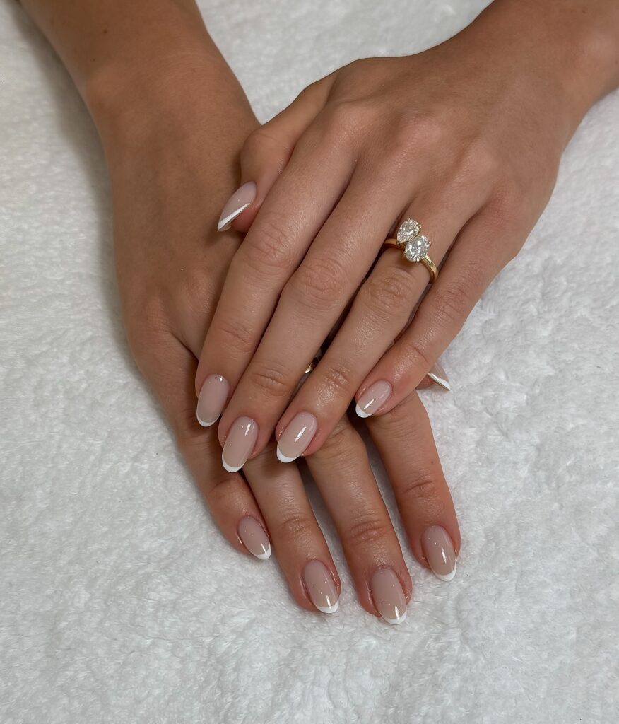 hands with short oval nails and clean white French tips on a sheer pink nude base