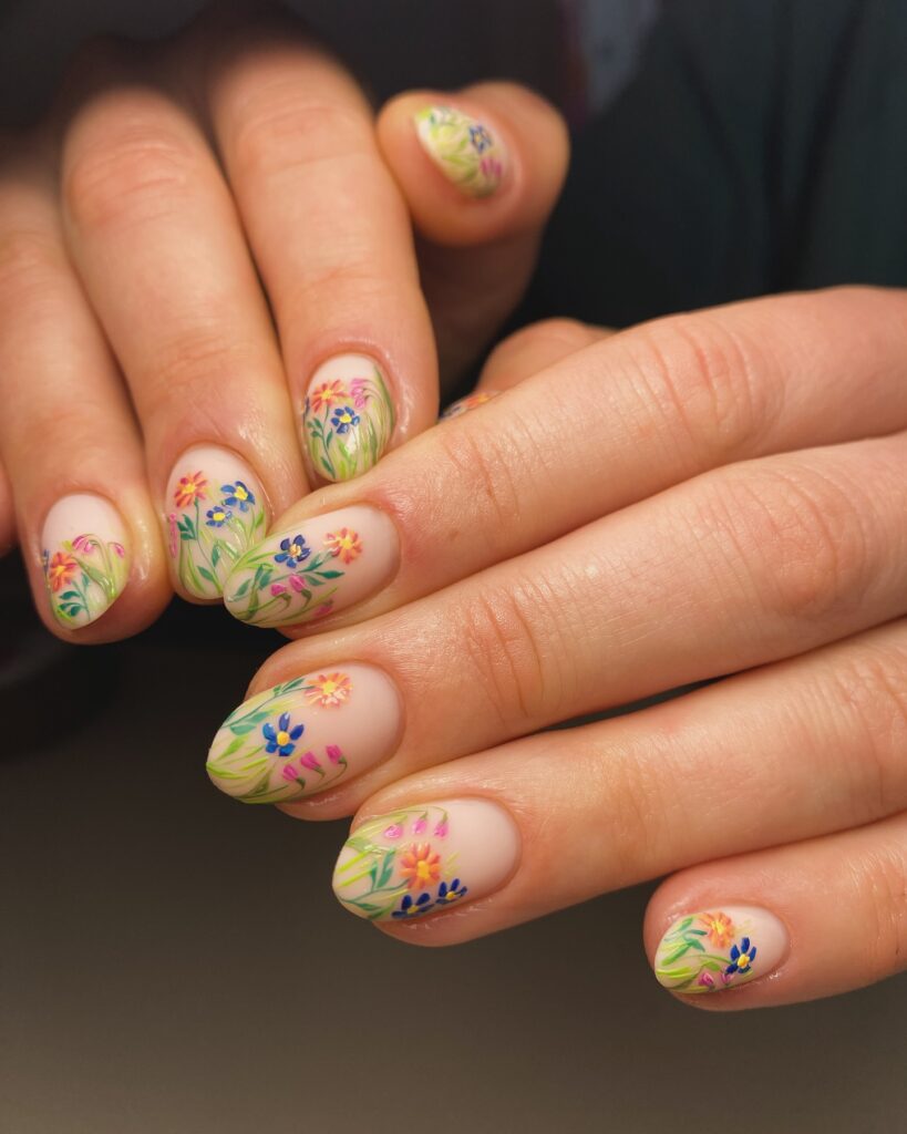 Short oval nails with sheer nude base and vibrant painted wildflower garden