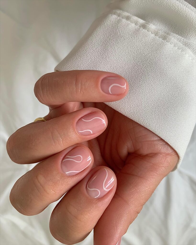 Short round blush pink nails with flowing white swirl line art on each nail