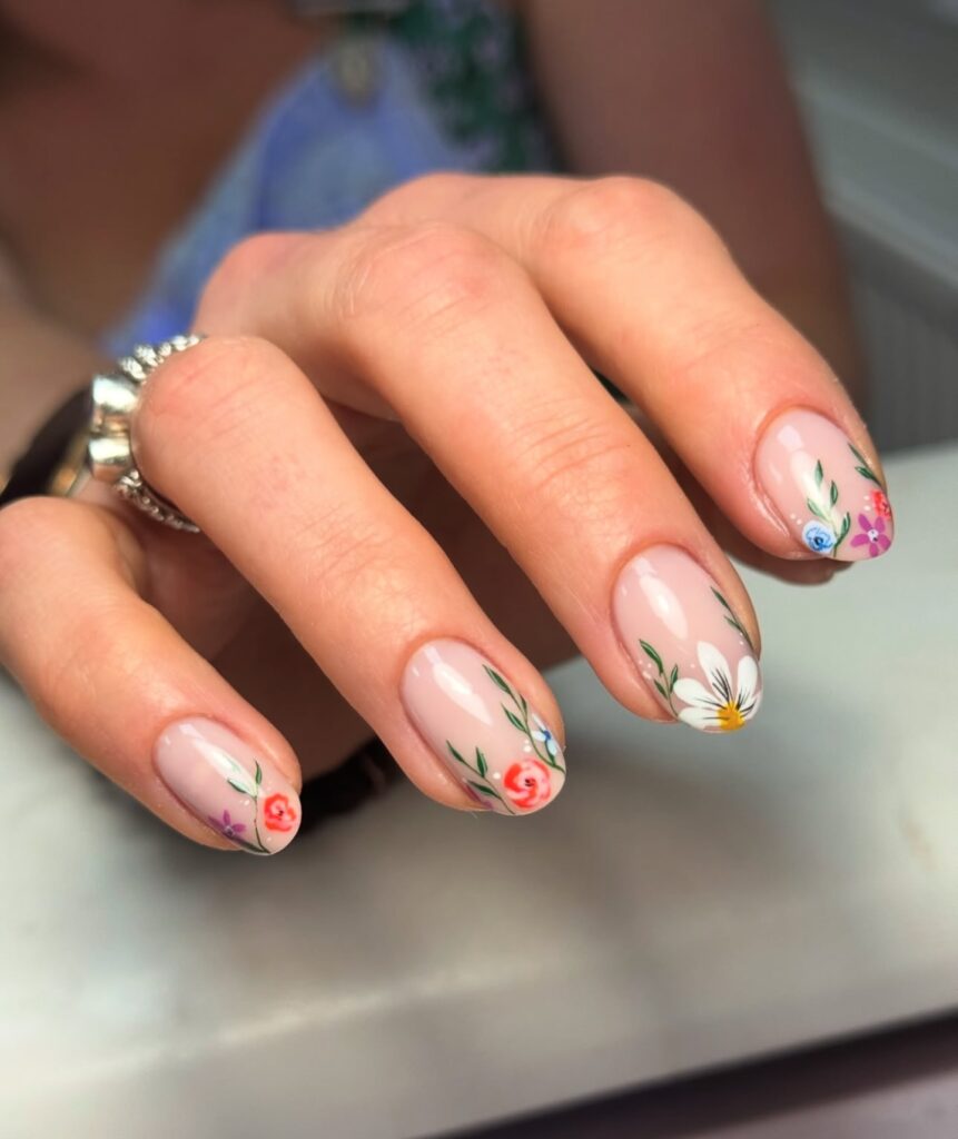 Short oval nails with sheer nude base and hand-painted garden flowers at corners