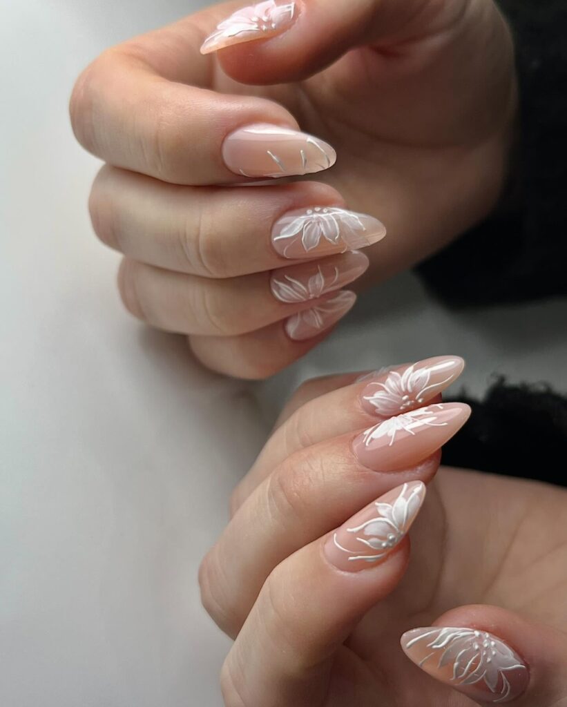Long pointed nails with sheer nude base and raised white botanical floral art