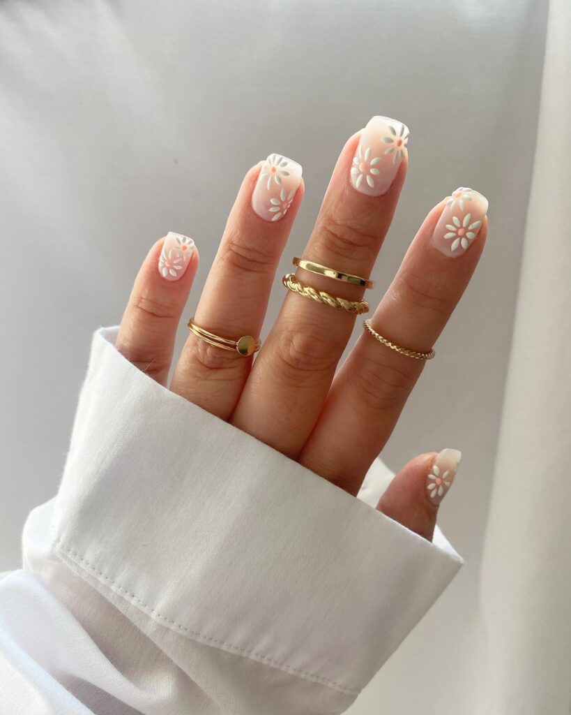 Short square white nails with bold embossed white daisy designs and peach centres