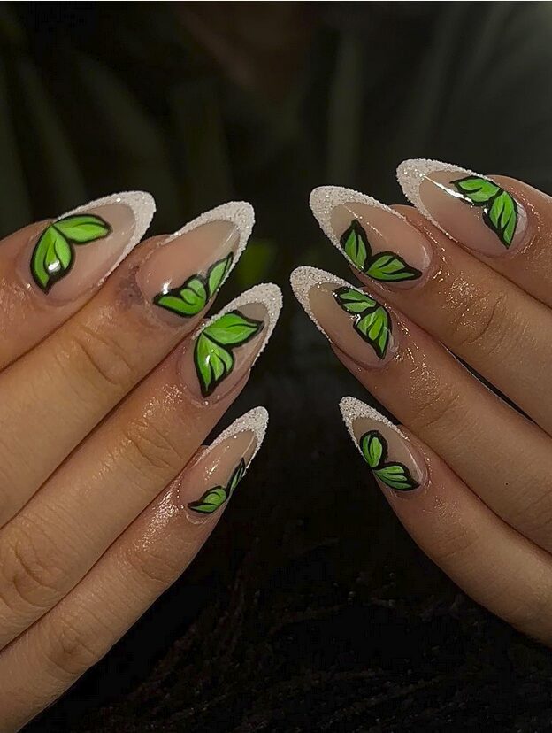 long nails with white sparkly French tips and bright green leaf accents