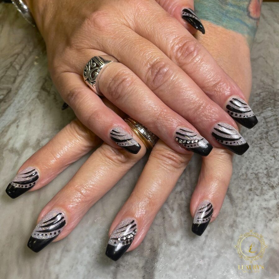 Black ombre nails with silver glitter accents, rhinestone details, and abstract swirl designs