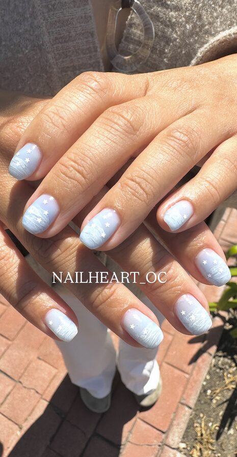 Light blue ombré nails with white star and cloud designs
