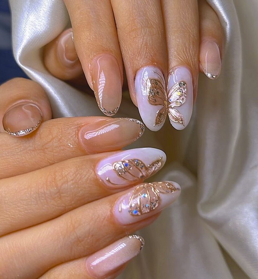 Nude and white nails with gold butterfly designs and glitter accents
