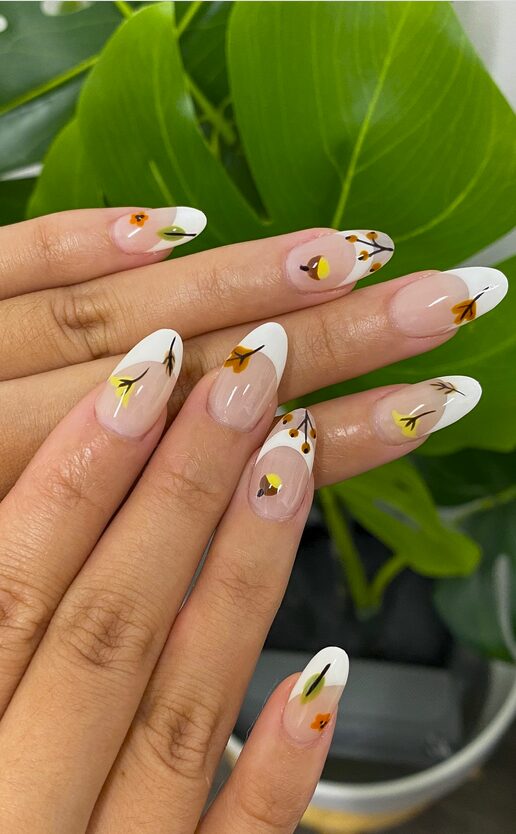 White French tip nails with small autumn-colored leaf designs