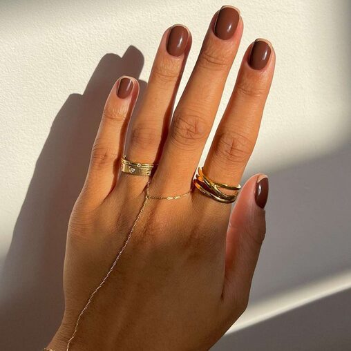Short glossy brown nails in natural light with gold rings
