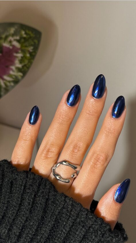 almond-shaped nails painted in a deep midnight blue chrome finish with a glossy metallic sheen