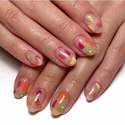 Close-up of hands with short, glossy nude nails decorated with colorful tiny fruit stickers
