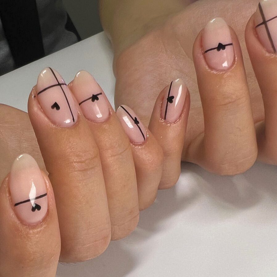 Minimal nude nails with thin black lines and tiny heart accents