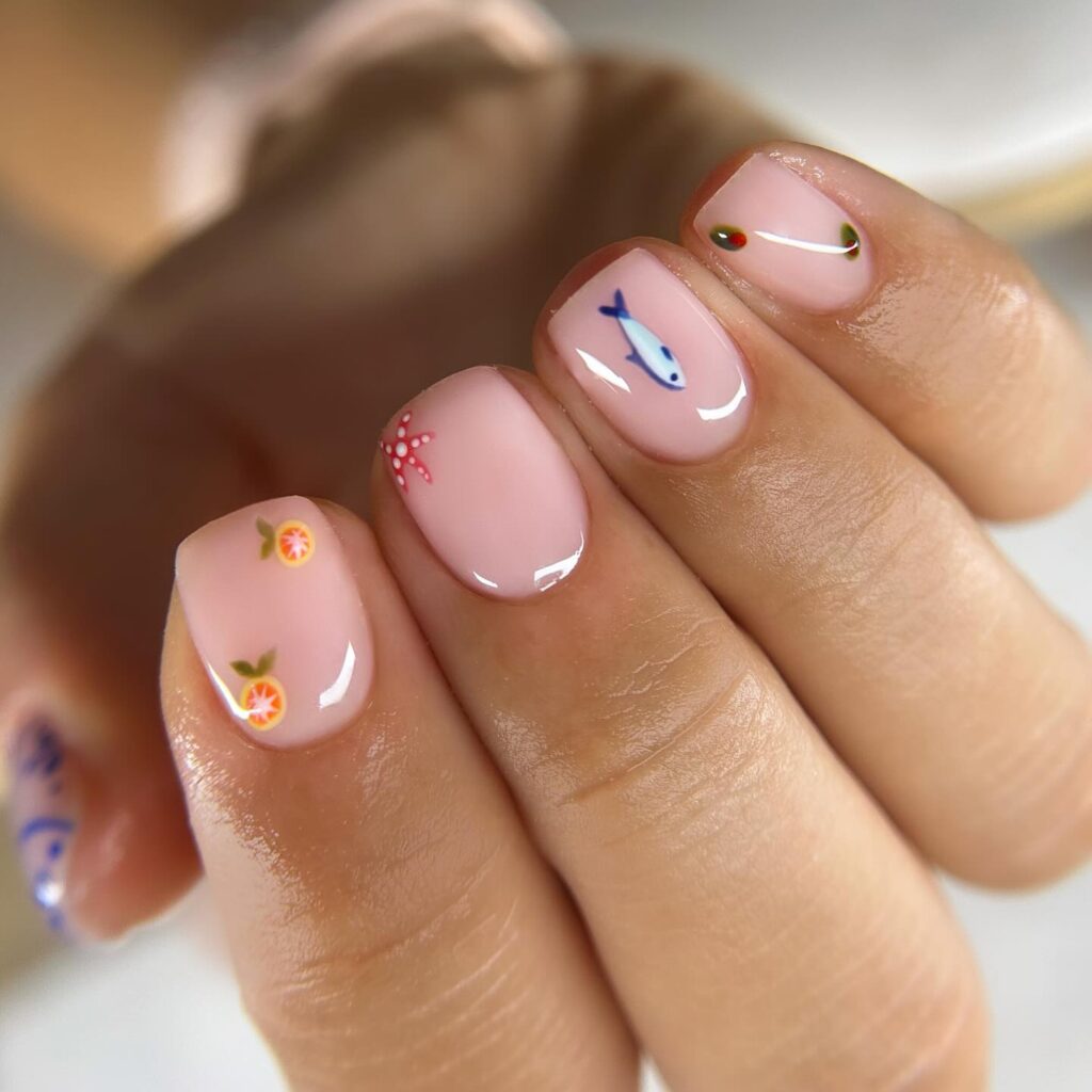 Glossy pale pink nails with tiny summer-themed art: orange slices, a starfish, a fish, and olives