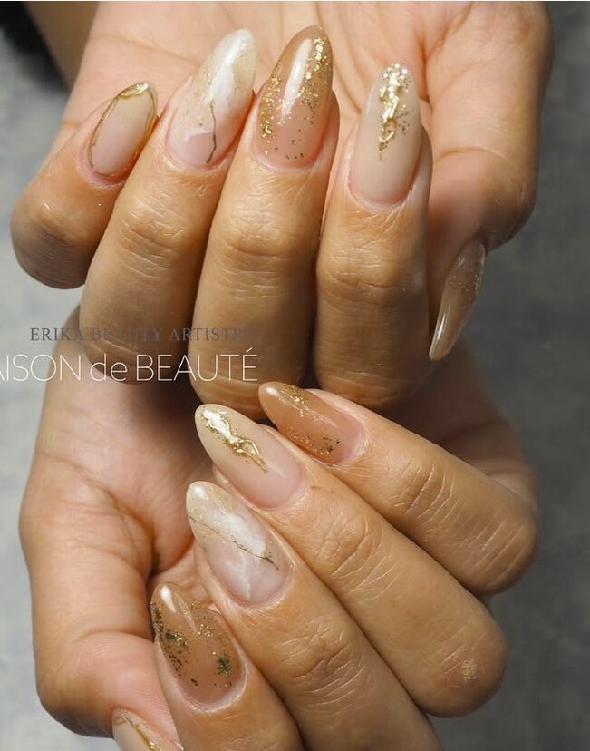 Beige and nude nails with marble effects, gold leaf accents, and a glossy finish