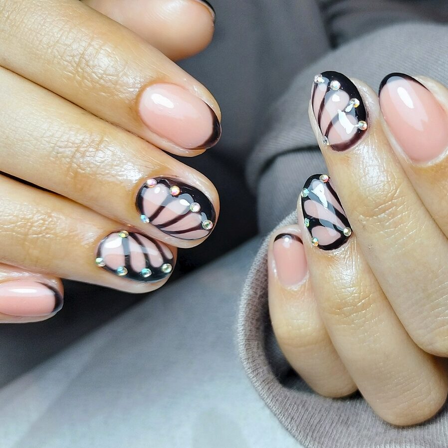Peach nails with black butterfly wing tips and rhinestone accents