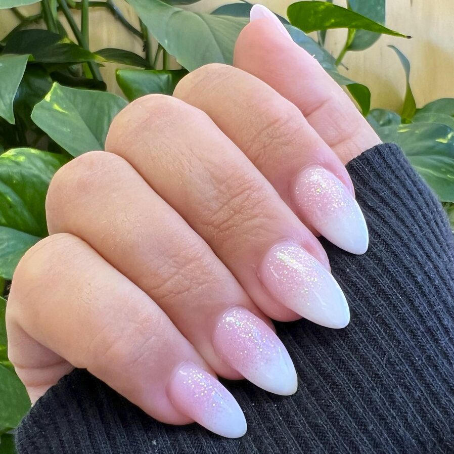 Pink to white ombre nails with subtle glitter on almond-shaped tips
