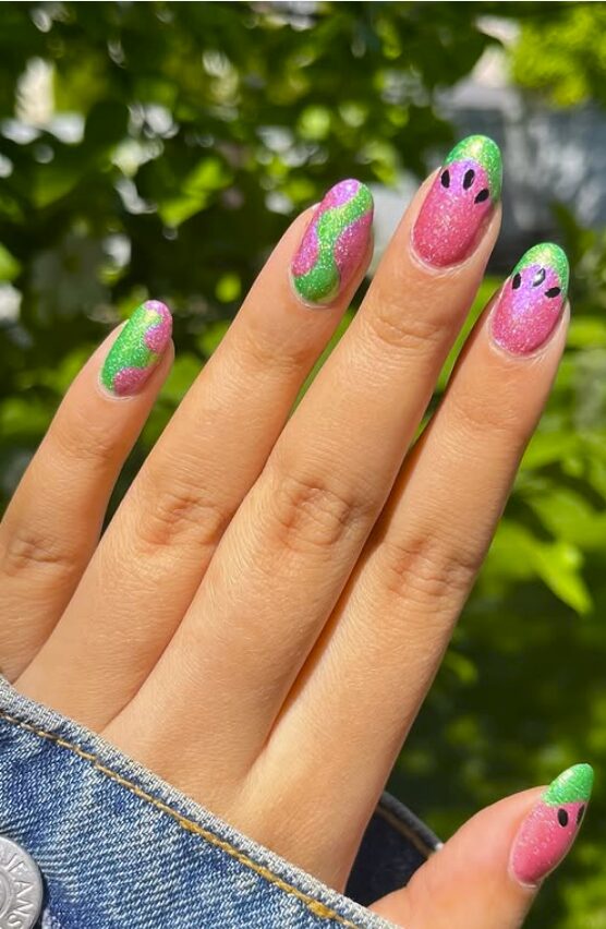 Pink and green glitter nails with wavy designs and watermelon seed accents