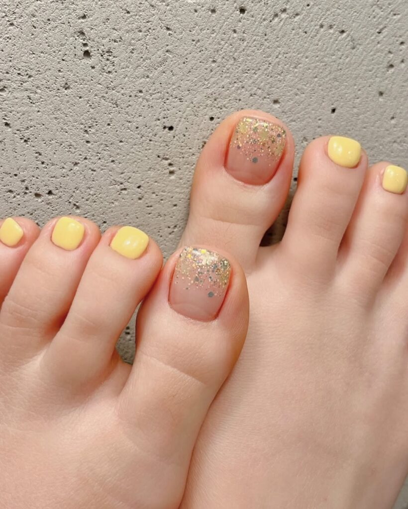 soft yellow spring toe nails with nude big toes and gold glitter accents