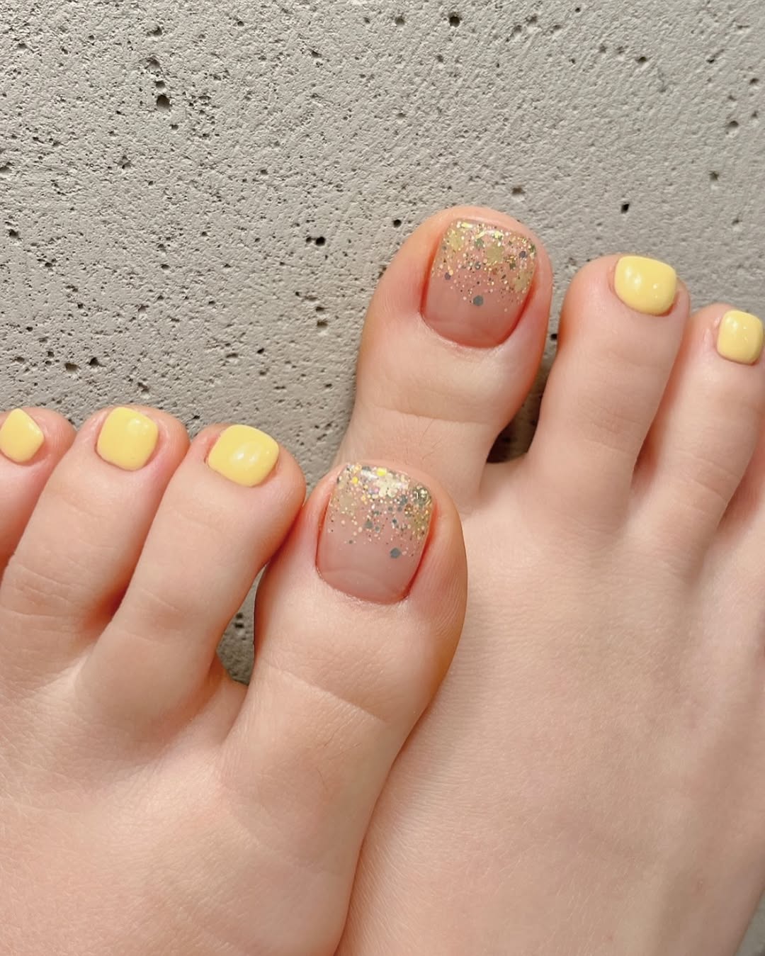 soft yellow spring toe nails with nude big toes and gold glitter accents