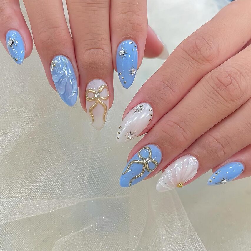 Blue and white 3D gel nails with gold bow accents and crystal details