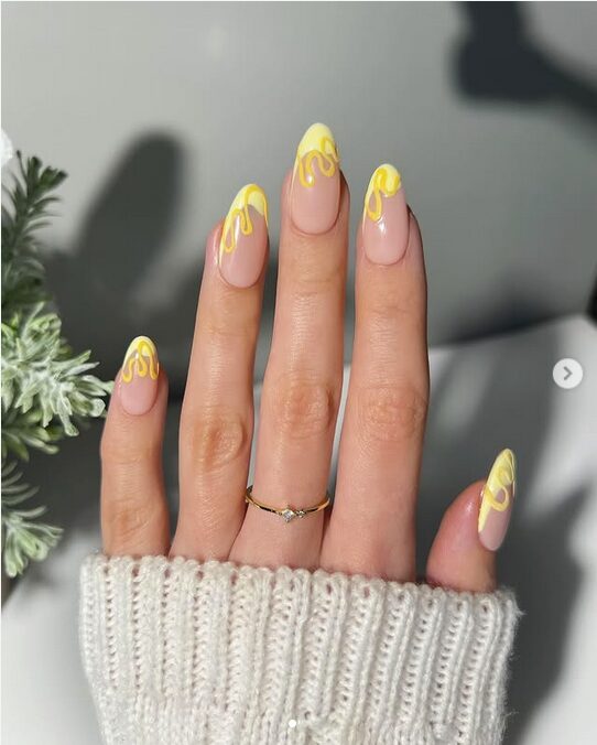 Almond nails with nude base and glossy yellow abstract swirls.