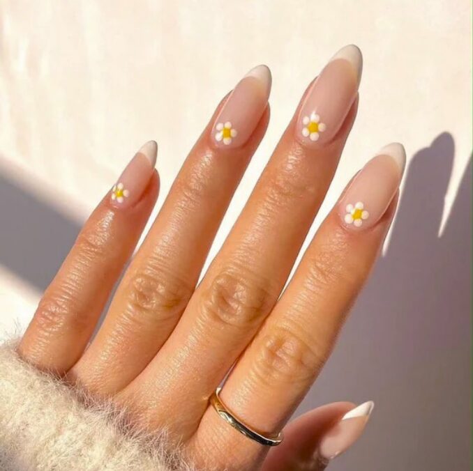 Nude nails with small white and yellow daisy designs.