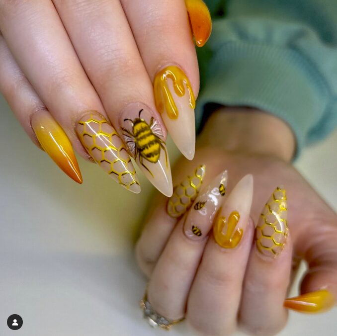 Long almond nails with honeycomb patterns, bee art, and glossy yellow drip designs