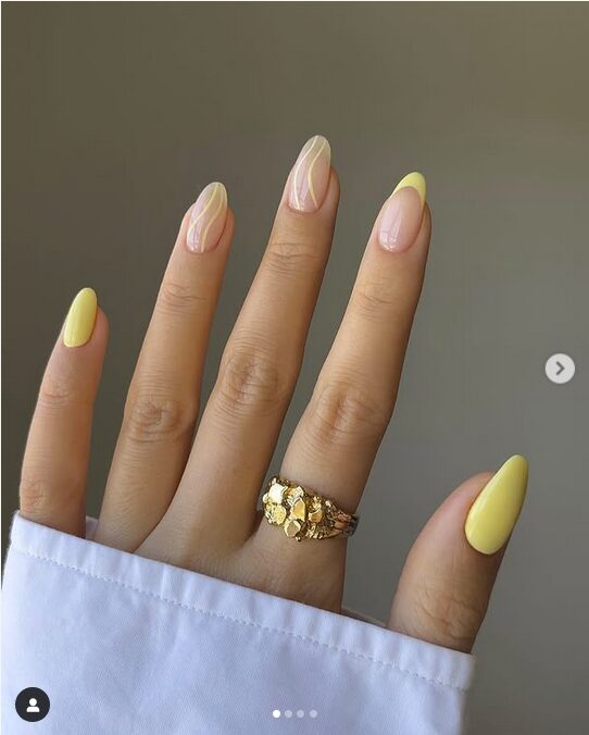 Pastel yellow nails with nude accent nails featuring white swirls