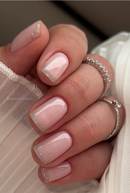 Short, glossy nude nails with subtle silver glitter tips
