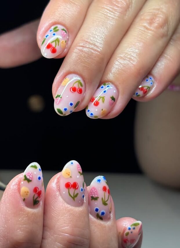 sheer pink nails decorated with hand-painted cherries, small flowers, and colorful confetti-style dots