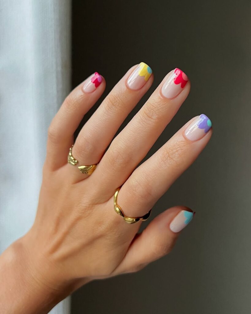 colorful flower-inspired French tips on a nude base in red, yellow, purple, and pastel blue