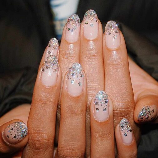 nude nails with silver glitter and star-shaped confetti concentrated on the tips