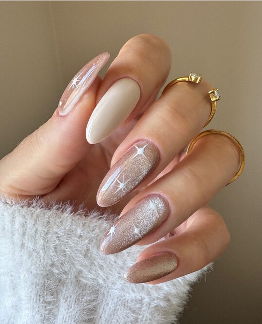 champagne glitter nails with white star accents and a nude matte accent nail