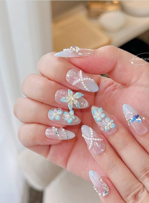 pastel nails with 3D blue flowers, pearls, crystal accents, and soft sheer bases