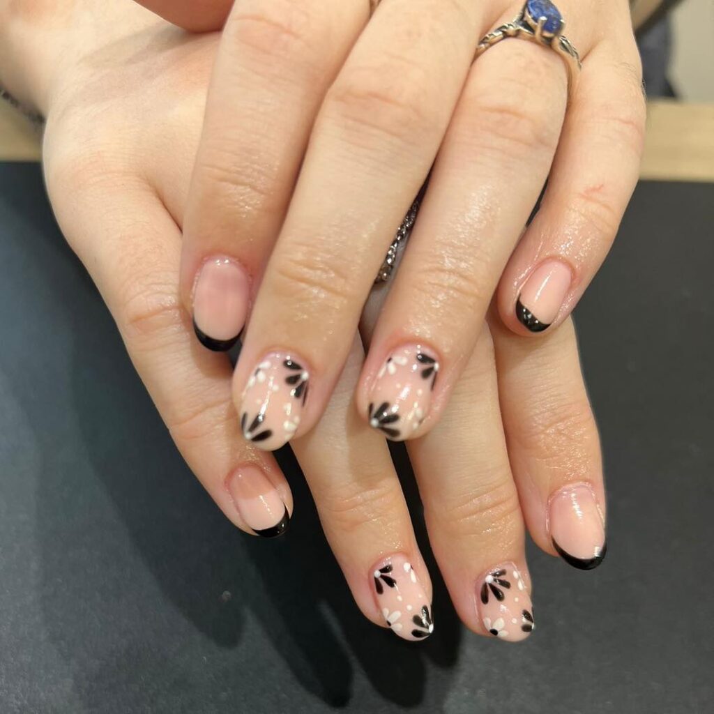 short oval nails with black French tips and hand-painted black floral dots
