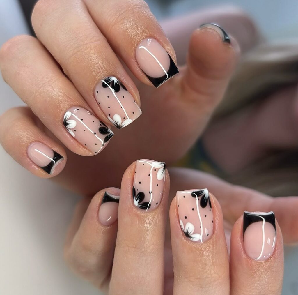 short square nails with black French tips, black and white floral designs, and polka dot accents