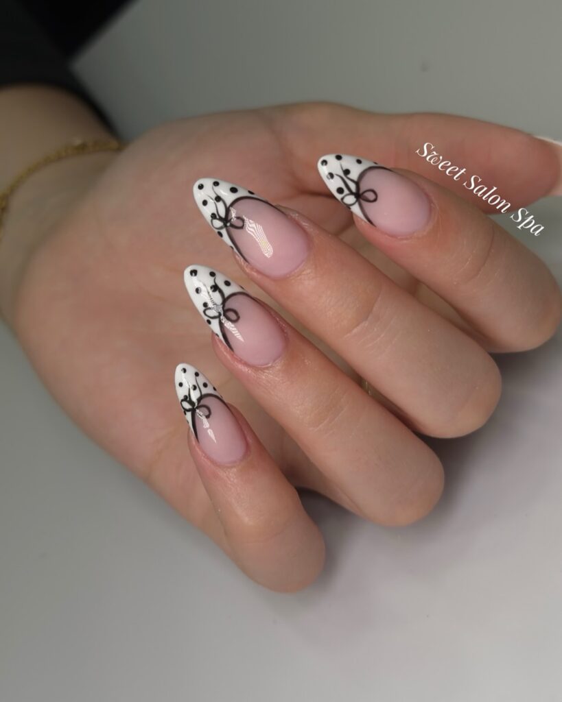 nails with white French tips featuring hand-painted black bow and lace vine nail art
