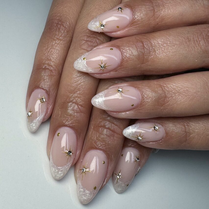 Shimmery white French tips with gold star accents on nude nails