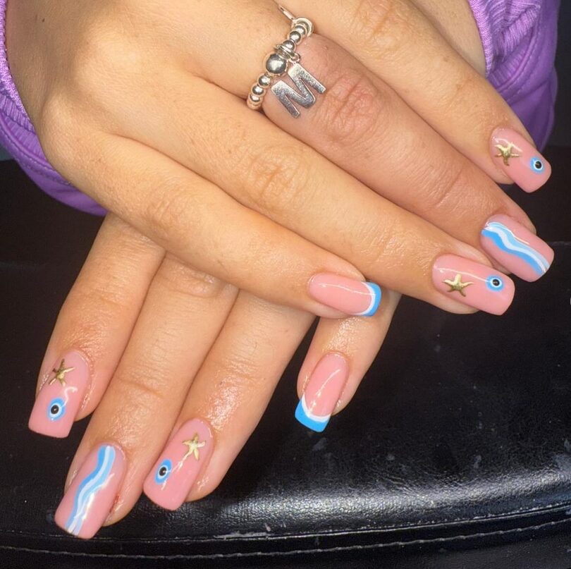 Blue French tips with wave designs, starfish charms, and evil eye accents