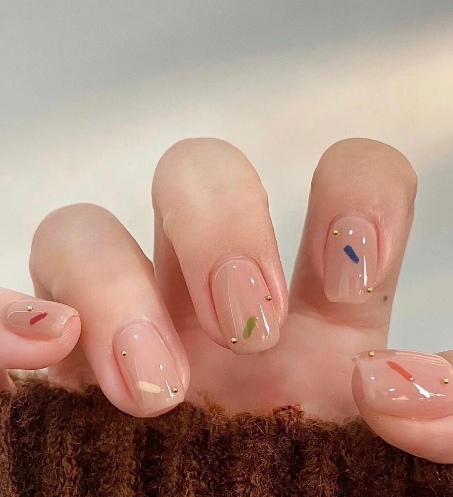 Glazed nude nails with brushstroke confetti and gold studs