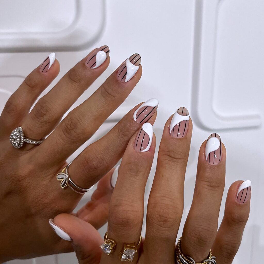 nails featuring a nude base with thin vertical black pinstripes and abstract white swirling accents