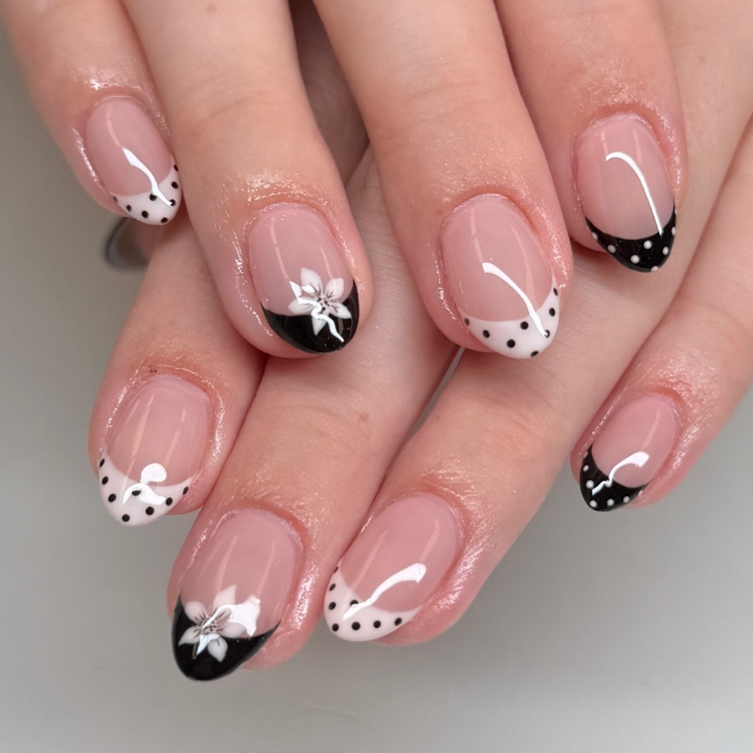 Almond nails with black French tips, white flowers and polka dots
