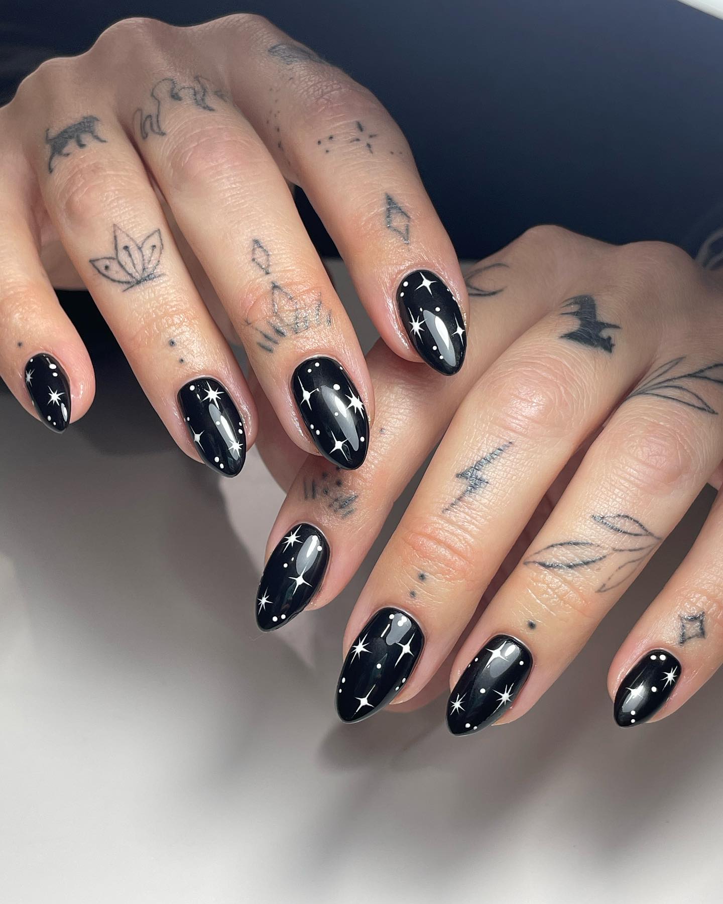 Glossy black almond nails with white star and sparkle accents