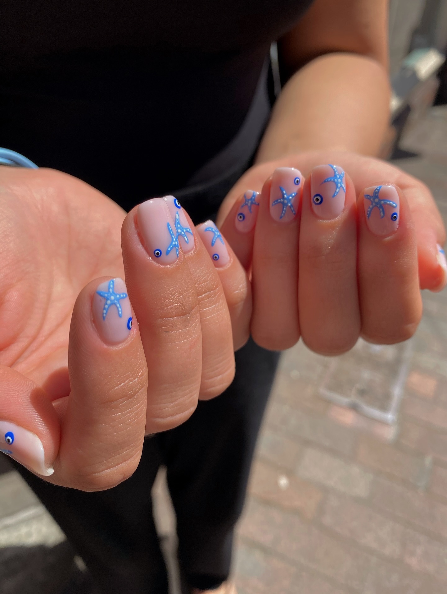 Blue starfish and evil eye motifs on short sheer nails