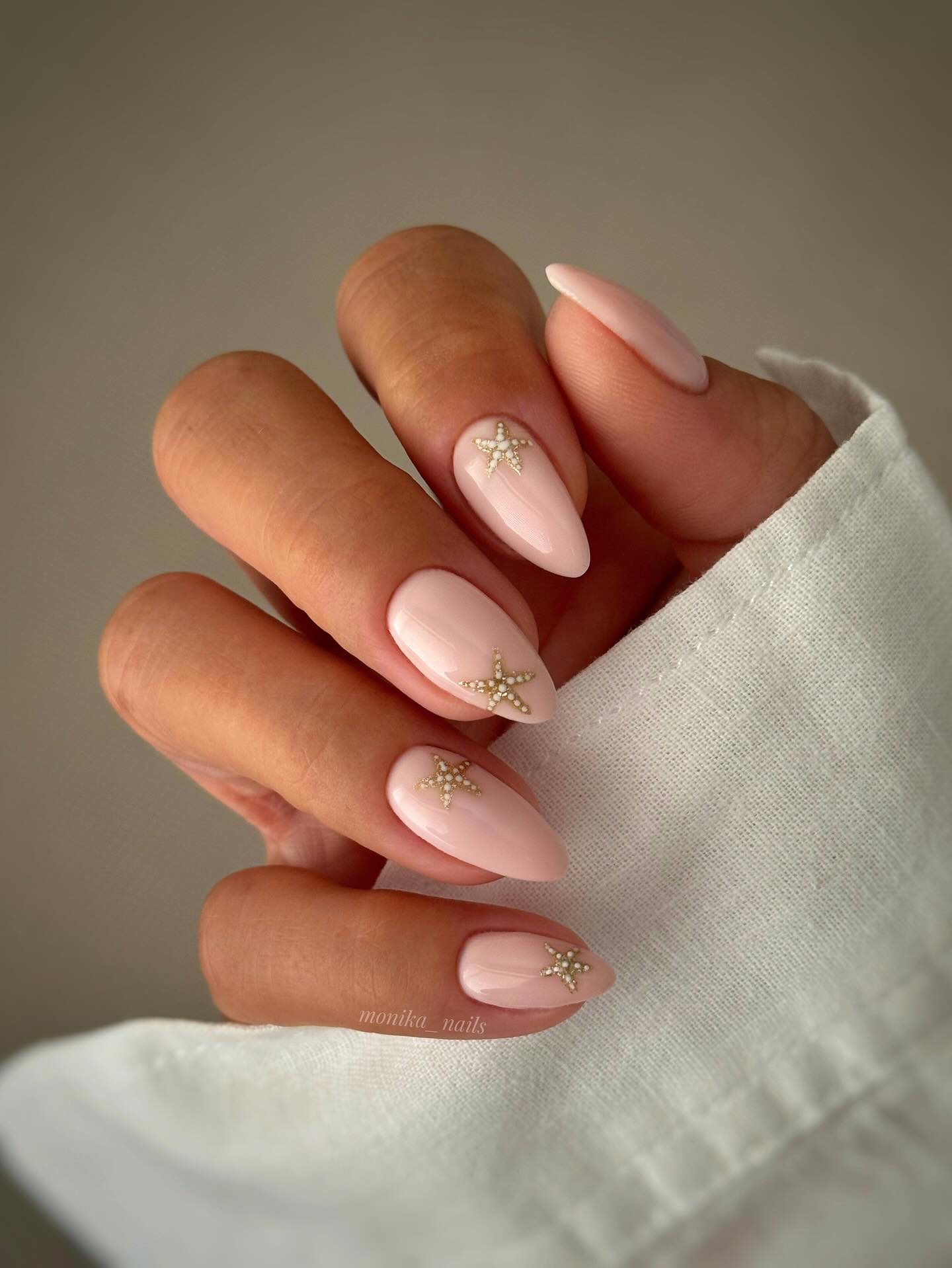 Blush pink almond nails with small gold and pearl starfish charms