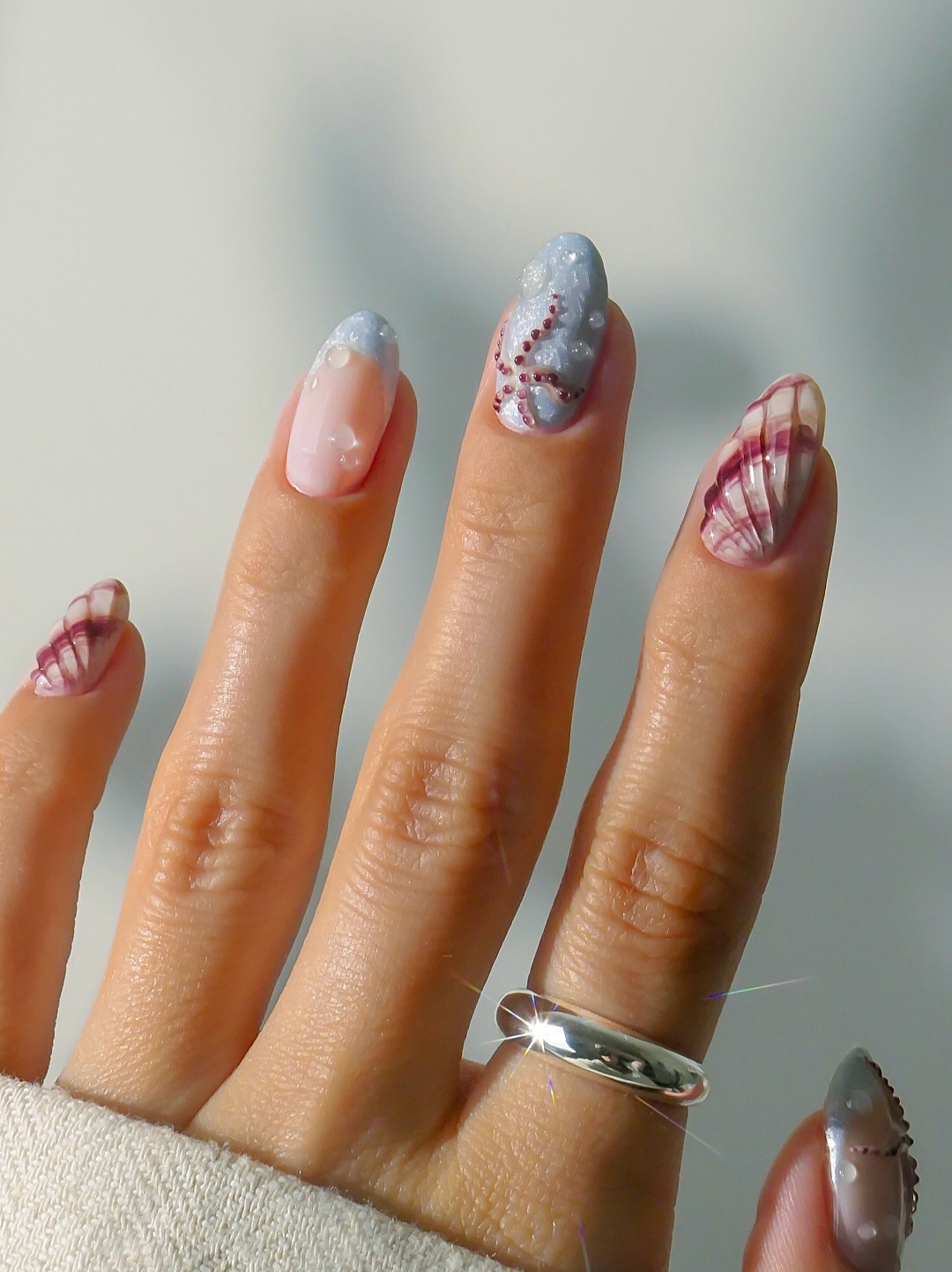 Dusty blue glitter nails with burgundy rhinestone waves and striped seashell art